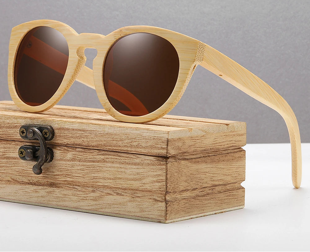Wooden sunglasses with brown lenses on a wooden box against a gray background, featuring the brand 'GM Eyewear'.